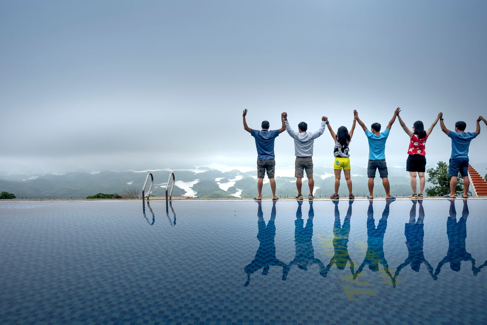 Friends raising their arms in celebration at the edge of an infinity pool, the kind of happy travellers cruise surveys ask about