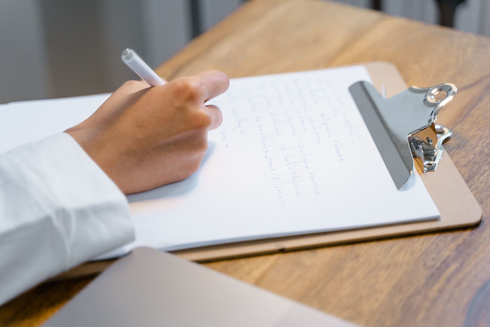 A hand writing on a clipboard on a wooden table